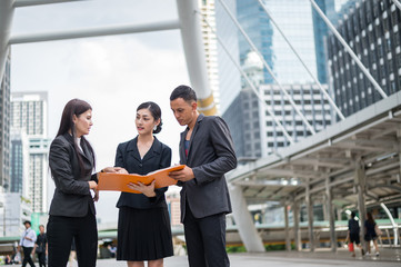 Fototapeta premium Asian business woman standing and holding financial document on hand, she talking about business future with businessman and team.
