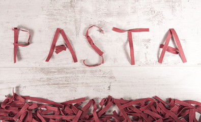 Pasta sign made with red color italian raw thick pasta maded from flour, eggs and beetroot on wooden background