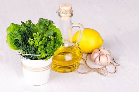 Fresh herbs in a bucket with lemon and olive oil on a light wooden background