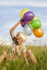 Young beautiful female with long blonde hair playing with color balloons in the middle of meadow