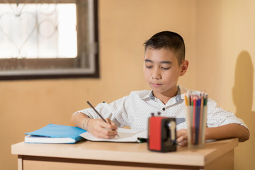 A Little Asian boy use pencil writing on notebook homework on wooden table. Back to School concept.