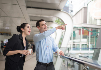 Two colleagues walking in street of city talking to each other while holding disposable coffee cups.