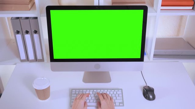 top view invisible woman working on computer. female fingers typing on white keyboard. workplace with paper cup of coffee on white table folders pc display with isolated green screen
