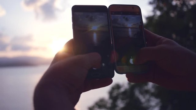 Male tourist removes from two hands on two phones a beautiful sunset on the sea. Slow motion. HD, 1920x1080