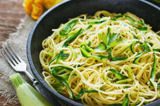 Pasta with zucchini on dark wooden background in a cast-iron frying pan . Spaghetti from organic wholegrain flour