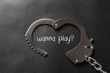 handcuffs shaped like a heart on black and writtting with wanna play - obrazy, fototapety, plakaty