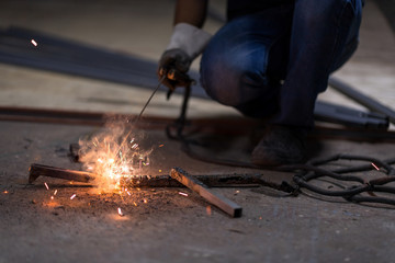 Selective focus at steel rod and Motion blur. Low light image of Welder or craftsman in a welding mask and welders leathers, a metal product is welded with a welding machine in the garage.