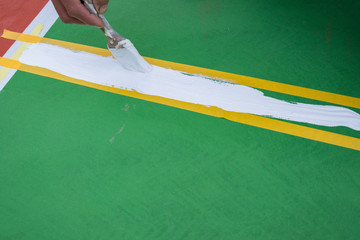 worker painting the sideline on the floor for an outdoor stadium