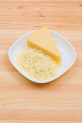 Close-up on a wooden table in a plate is Parmesan cheese in grated and brick form. The concept of solid dairy products