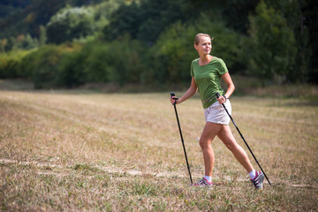 Pretty, young woman nordic walking on a forest path, taking in the fresh air, getting the daily...