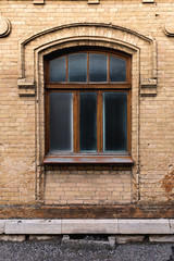 Vintage arched window in the wall of yellow brick. Black glass in a maroon dark red wooden frame. The concept of antique vintage architecture in building elements.