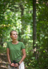Pretty, young woman nordic walking on a forest path, taking in the fresh air, getting the daily...