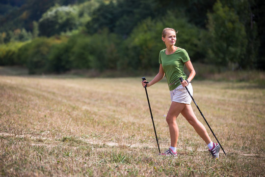 Pretty, young woman nordic walking on a forest path, taking in the fresh air, getting the daily dose of exercise
