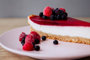 cheesecake with jelly and berries on a pink plate around which berries lie on a wooden table