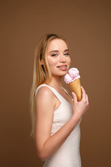 girl with braces on her teeth in a pink dress holds a pink ice cream and smiles on a beige background