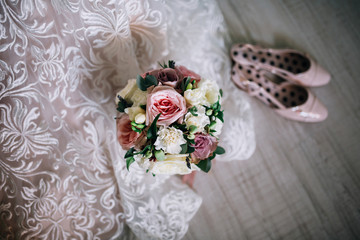 wedding bouquet of roses and peonies and greens with lavender on the background of a wedding lace dress and pink shoes on a wooden background