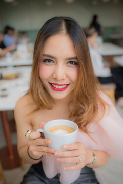 beautiful woman smile and holding a cup of coffee in her hand on blur background coffee shop