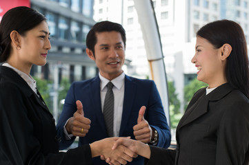 business man show thumb up and two business woman shaking hands and smile for demonstrating their...
