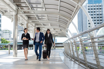 businessman and businesswoman walk together and talk about business with mobile and luggage on the public street, business travel