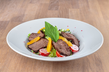  slices of boiled beef with lettuce, cherry tomatoes and orange pulp on a plate stand on an oak table