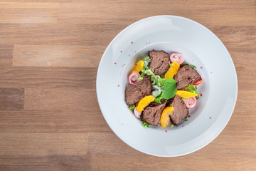  slices of boiled beef with lettuce, cherry tomatoes and orange pulp on a plate stand on an oak table