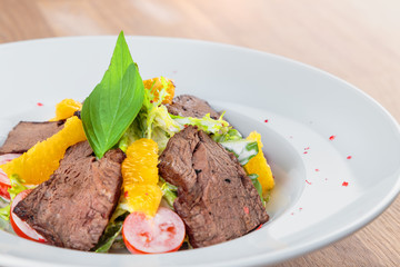  slices of boiled beef with lettuce, cherry tomatoes and orange pulp on a plate stand on an oak table