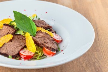  slices of boiled beef with lettuce, cherry tomatoes and orange pulp on a plate stand on an oak table