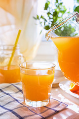 Juicy orange juice in a glass and jug and ripe fruit orange on a white table near the window, the concept of breakfast on a sunny summer day