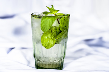 Fresh mint water with ice cubes on a white surface with fresh organic mint leaves.