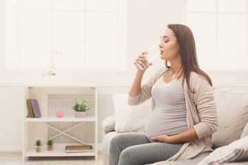 Pregnant woman drinking water sitting on sofa