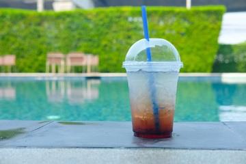 Soda with ice at the edge of a pool.
