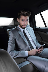 man in suit sitting in car and reading messages on smartphone