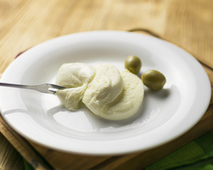 Cheese mozzarella and olives on a plate on a wooden background.