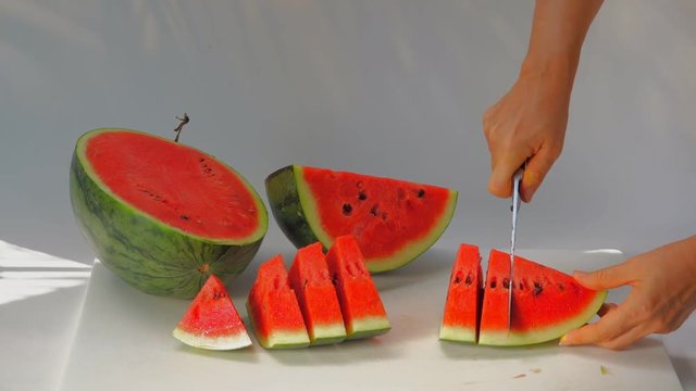 Watermelon for refreshment.
Woman cutting red juicy watermelon into sliced , HD slow motion white background.
