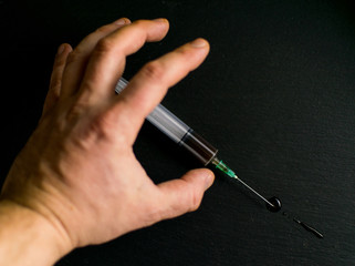 The concept of drug addiction. The hand reaches for the syringe against a dark background.