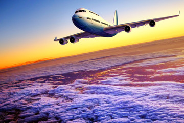 Airplane flying above clouds at sunset.