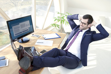 Successful young businessman at the office. Full length shot of successful young business man wearing suit while sitting at his modern office with his legs on office desk.