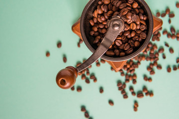 Coffee beans in a hand-held coffee grinder on a tender green background top view