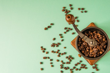 Naklejka premium Coffee beans in a hand-held coffee grinder on a tender green background top view
