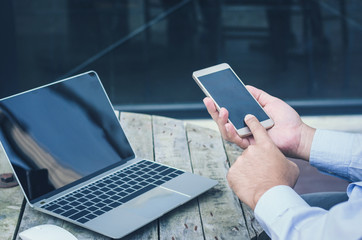 attractive handsome business man touching on smartphone and using computer laptop working on wooden table at outdoor.