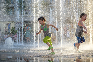 Happy kids have fun playing in city water fountain on hot summer day. - Powered by Adobe