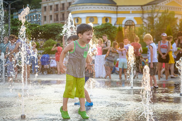 excited boy having fun between water jets, in fountain. Summer in the city