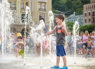 excited boy having fun between water jets, in fountain. Summer in the city