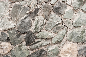 Close-up wall of  uneven rough uncouth gray stones.