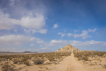 Long sandy dirt road leads down to a hill made of rock boulders.