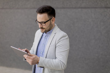 Young businessman with digital tablet by the grey wall