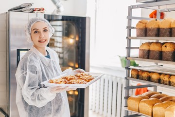 Girl Baker in white uniform holding a baking tray with pizza