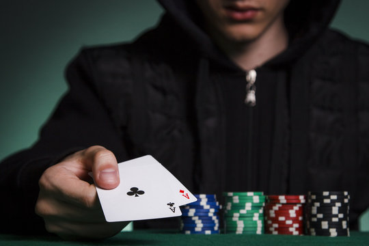 A guy in a black jacket holds a pair of aces against a pile of poker chips