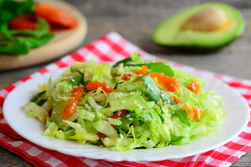 Fresh сabbage salad with avocado. Homemade cabbage salad avocado, dried apricots, arugula and sesame on a plate and on a wooden table. Raw vegetable salad. Raw food diet. Closeup