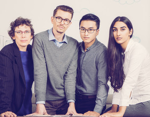 Business team of four serious people standing at table, working and looking at camera